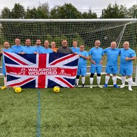 A team of footballers from Glasgow holding a WWTW branded Union Jack in front of goal posts